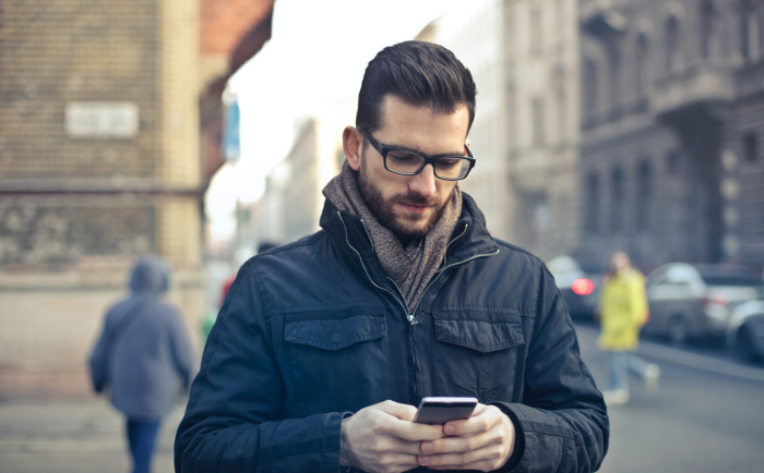 A man in a winter coat, using his phone on a sidewalk in the city.